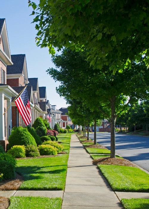 Tree-lined residential street with manicured lawns and landscaped front yards.