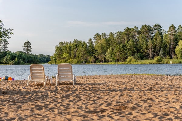 Sandy beach with lounge chairs overlooking Lake Minnetonka and pine trees.