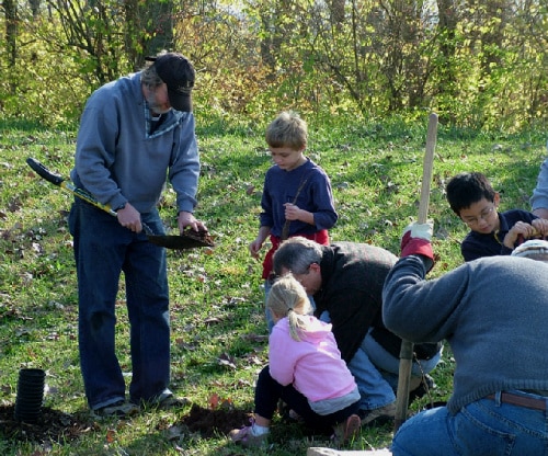 Ostvig crew members and children planting a tree together in a grassy area.